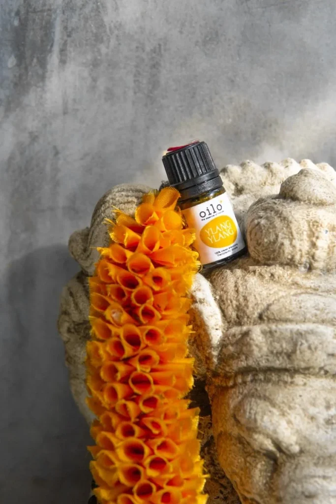 Buteleczka olejku ylang ylang na kamieniu obok pomarańczowego kwiatu